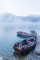 Wooden boats by the pier on a lake at sunset with mist rising over the water