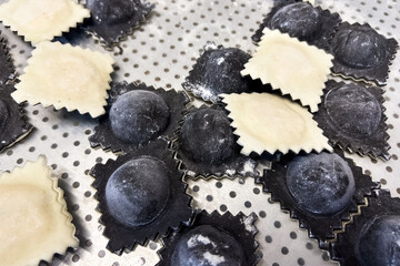 Homemade ravioli filled with cheese and herbs on a metal tray ready for cooking