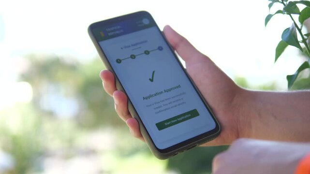 Against a natural backdrop, a man's hands use a visa application service on a smartphone, pressing the submission button and receiving a successful application notification. 