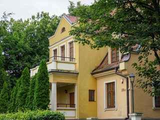 Traditional yellow European house with a large balcony and green trees on a summer day