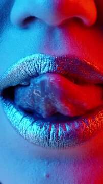 Vertical slow motion macro of glossy metallic lips licking upper lip under neon blue red light, sensual beauty and fashion concept symbolizing temptation glamour confidence and modern aesthetic