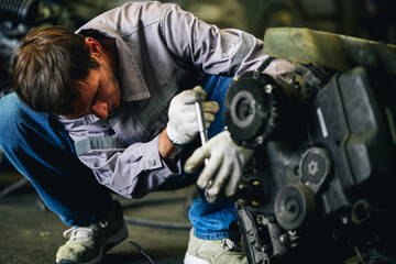 White man technician checking used car damaged engine block at scrap yard warehouse recycle area part. Maintenance engineer inspecting rust oily auto motor old spare part in junkyard for reuse service