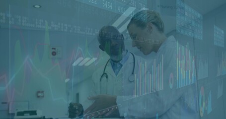 Reviewing metrics, two doctors analyzing digital charts in hospital hallway with stethoscopes