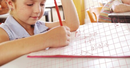 Writing math equations boy sitting at school desk on graph paper in classroom, with red pencil