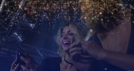 Friends checking smartphone in blue nightclub under truss and spotlights, golden sparkle overlay