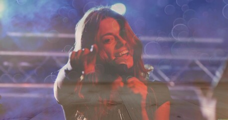 Singing singer holding handheld mic reaching toward audience on music stage with truss lights, haze