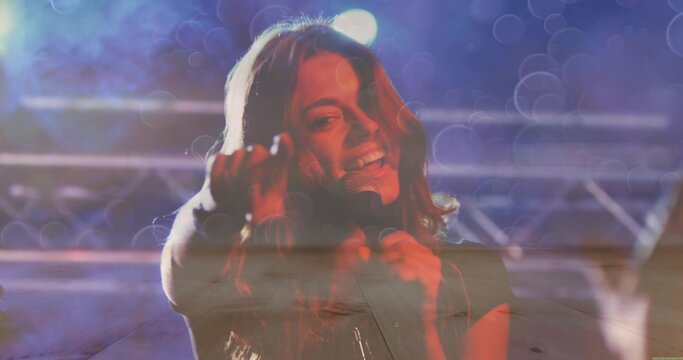 Singing singer holding handheld mic reaching toward audience on music stage with truss lights, haze