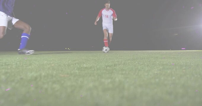 Soccer player 14 dribbling ball on lit turf evading tackle jumping colliding helping defender