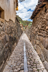 Traditional narrow alleyway with ancient Inca stone walls and cobblestone pavement in the historic town of Ollantaytambo, Peru.