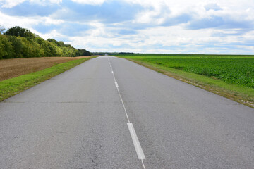 Long Straight Road Through Rural Fields Under Cloudy Sky