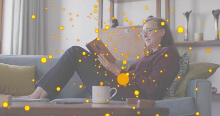 woman opening pages of book on gray sofa and releasing glowing particles for immersive learning - Powered by Adobe