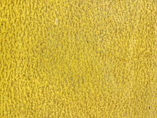Bright yellow plaster wall texture with a wavy pattern due to its faded paint. Ideal for an abstract construction background or overlay