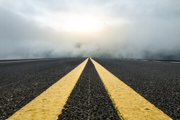 Asphalt road with yellow lines disappearing into foggy distance under bright sky