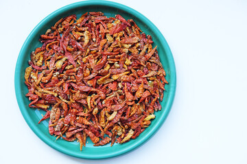 A top-down flat lay of dried red chili peppers in a turquoise plastic bowl, isolated on a clean...