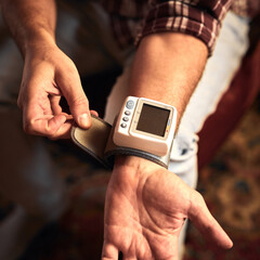 Man checking blood pressure and heart rate at home with a portable modern digital meter.