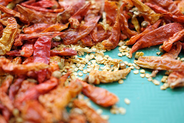 A macro shot of dried red chili peppers and their seeds scattered on a textured turquoise surface. The shallow depth of field focuses on the spicy seeds in the center.