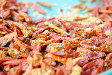 A macro photograph with a shallow depth of field, focusing on the wrinkled texture of a pile of dried red chili peppers on a turquoise tray.