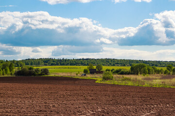 Freshly tilled brown soil stretches under a bright blue sky. Distant green fields and a dense...