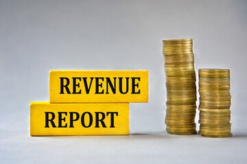 REVENUE REPORT - words on yellow wooden blocks on the background of stacks of coins