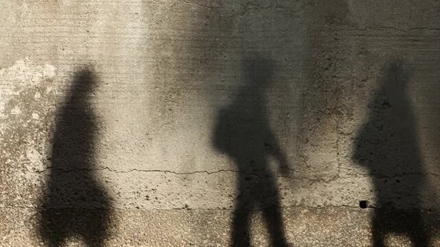 Silhouettes of pedestrians casting shadows on city street wall
