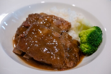 Pork rib with gravy sauce on rice, served on plate
