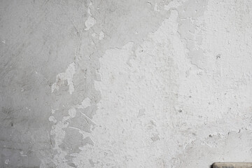 A close - up of a white concrete wall with peeling paint, showing a rough and weathered texture.