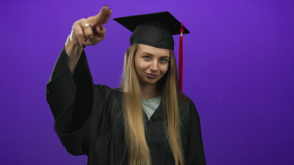 Young woman in graduation uniform posing confidently against an isolated purple background,...