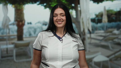 Woman smiling outdoors at a resort pool in a sunny, relaxing setting, highlighting vacation vibes...