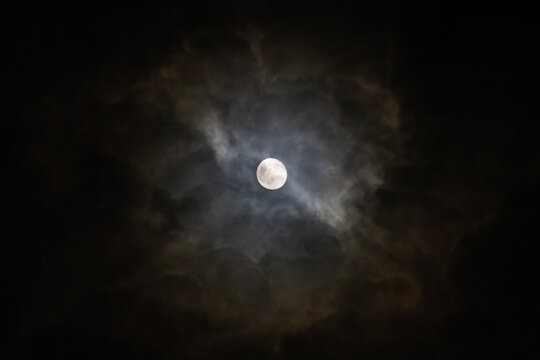 Full moon glowing through dark dramatic clouds at night
