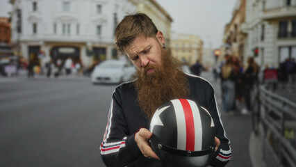 Young man with long beard holding a black and white striped motorcycle helmet on a busy urban street  introspection. © Krakenimages.com