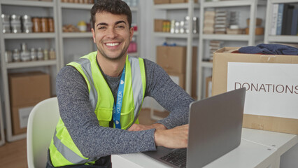 Man loads laptop for typing tasks at center computer station while hispanic young volunteer sorts donations for charity.