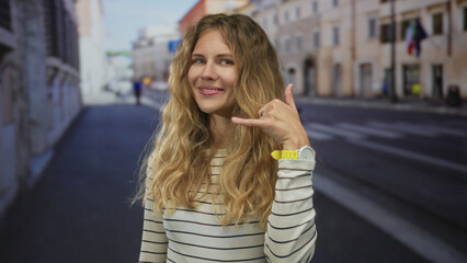 Fototapeta premium Woman holds hand pointing on a street and performs a blonde young gesture toward camera before making a call sign.