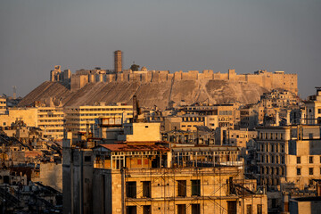 Fototapeta premium Close-up view of the Citadel of Aleppo at sunset. The ancient fortress stands majestically atop its hill, bathed in warm golden light. Its massive stone walls and towers reflect centuries of history.