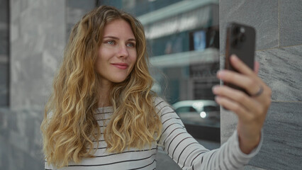 Fototapeta premium Woman holds smartphone while waving down a street before taking a selfie with a blonde young smiling kiss outdoor vibe.