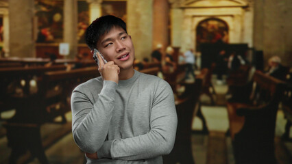 Young man in a church talking on smartphone wearing casual clothing, surrounded by wooden pews in a spiritual and serene indoor setting.