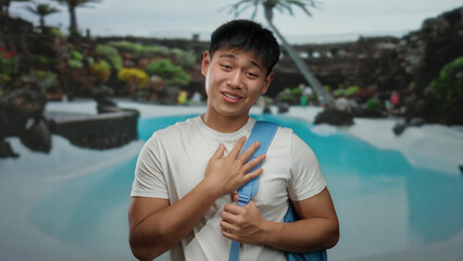 Young man with backpack smiling warmly at luxury outdoor pool in resort setting with tropical...