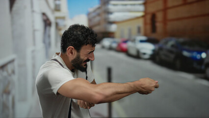 Hispanic man with beard mimics pulling a rope energetically on an urban street with blurred...