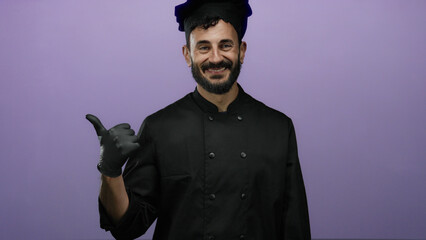 Obraz premium Hispanic bearded chef in black attire smiles against a vibrant purple backdrop, conveying a sense of culinary pride and inviting warmth with a thumbs-up gesture.