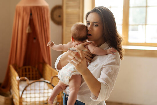 Babies and fever. Shocked mother looking at thermometer with high kid's temperature and holding infant baby on hands. Child care and infant's health problem concept