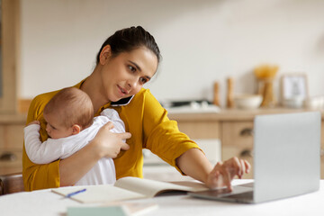 Busy mother caring baby having business phone call, sitting at table and using laptop. Remote job from home, babysitting and telecommuting