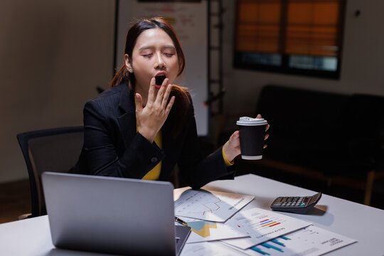 Tired asian woman with coffee working late in night at the office
