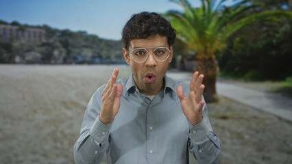 Young hispanic man wearing a light blue shirt with palms on cheeks and open mouth in building;...