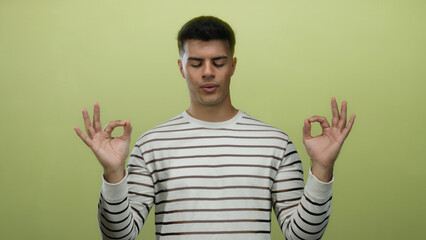 Young man meditates with closed eyes on yellow background, wearing striped shirt, conveying...
