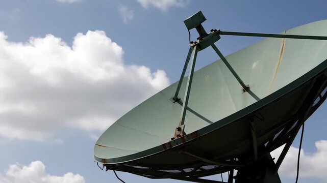 Large satellite dish angled towards a bright, cloudy sky, symbolizing communication and connectivity.