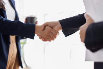 Two business people professionals shaking hands in office setting, sealing a deal with laptop and financial graphs visible. Business handshake over laptop and reports
