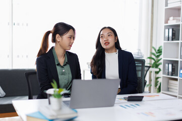 Fototapeta premium Two women having a business meeting in an office at sunset with financial documents and a laptop 