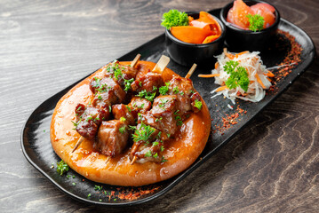 Grilled meat skewers on flatbread with sauce, pickled vegetables, and cabbage salad. Gourmet presentation on black plate. Top view, restaurant-style serving.