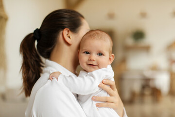 Child care concept. Young mother holding infant kid on hands, beautiful little baby smiling looking at camera at home