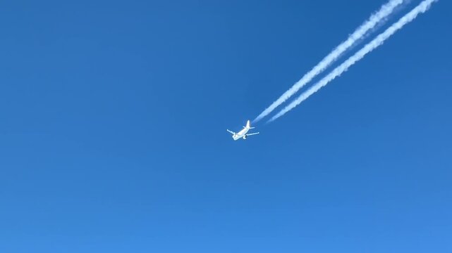 Aerial view of a white jet flying at high altitude and its wake in a blue sky 4k 
