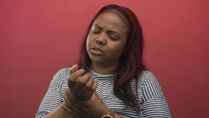 Woman holding wrist in red studio while wearing striped shirt with closed eyes and frown showing...